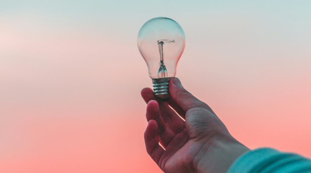 Χέρι κρατά μία λάμπα  με φόντο τον ουρανό