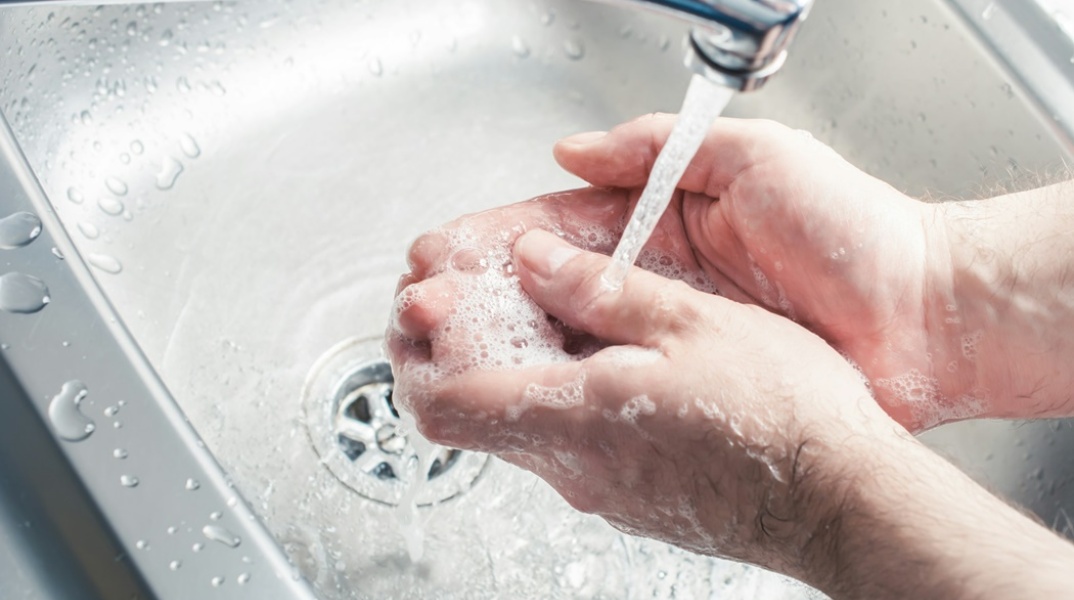 Νερό που τρέχει από βρύση ενώ άτομο πλένει χέρια
