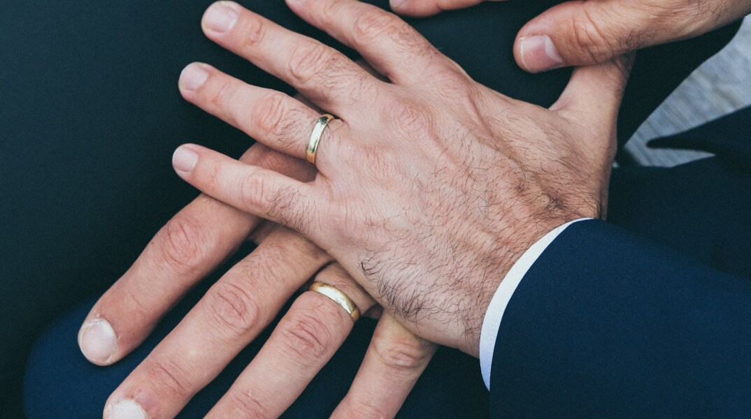 Χέρια δύο ανδρών που φορούν βέρες - Εικόνα που παραπέμπει σε γάμο