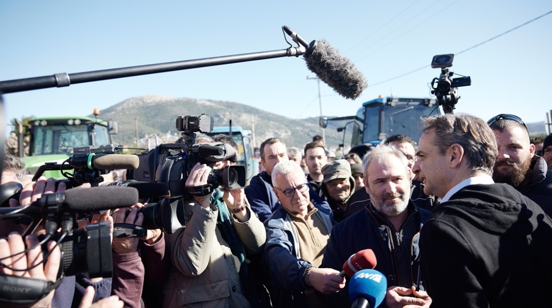 Ο Κυριάκος Μητσοτάκης κάνει δηλώσεις στα τηλεοπτικά συνεργεία ενώ στο βάθος της φωτογραφίας υπάρχουν παραταγμένα τρακτέρ
