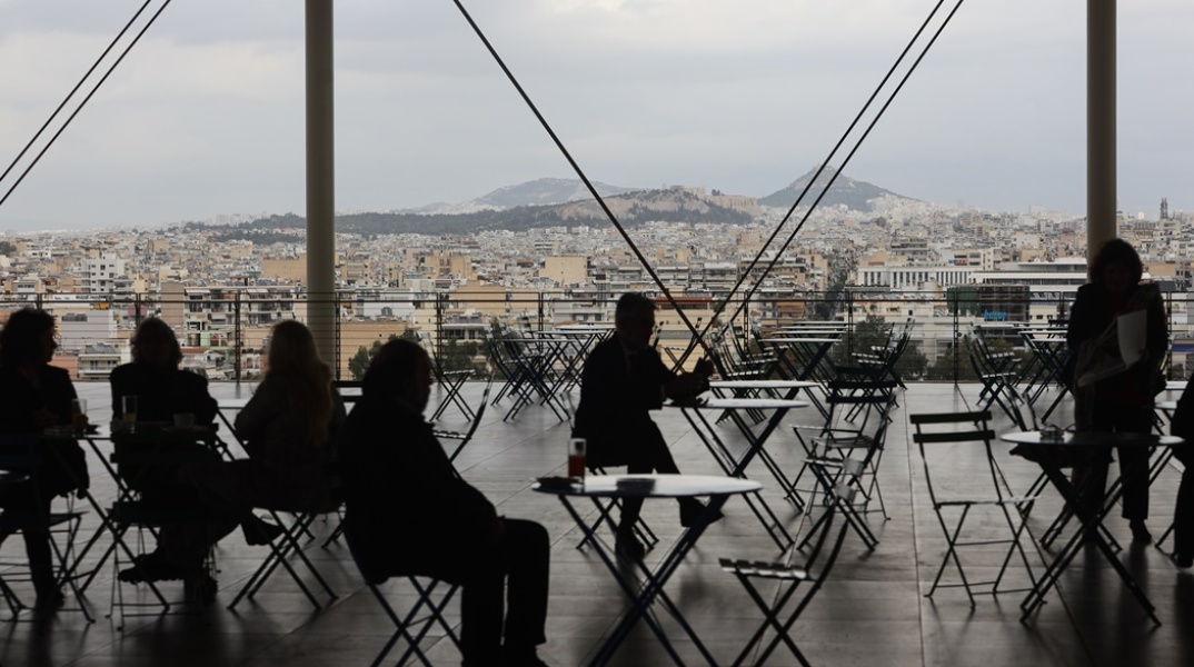Συννεφιά και άτομα που κάθονται σε τραπεζάκια στο Κέντρο Πολιτισμού Ίδρυμα Σταύρος Νιάρχος