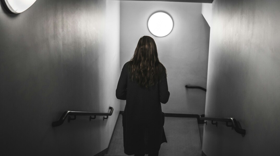 Γυναίκα, με την πλάτη γυρισμένη στον φακό, περπατά σε σκοτεινό διάδρομο