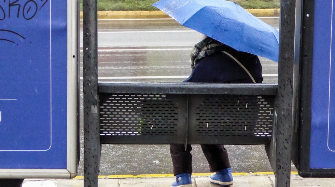 Γυναίκα με ομπρέλα σε στάση λεωφορείου ενώ βρέχει