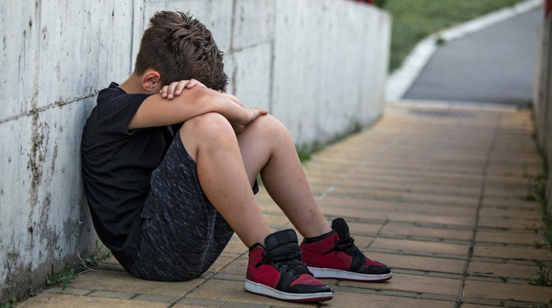 Αγόρι καθισμένο με τα χέρια να αγκαλιάζουν τα γόνατά του - Εικόνα που παραπέμπει σε άτομο που έχει υποστεί bullying