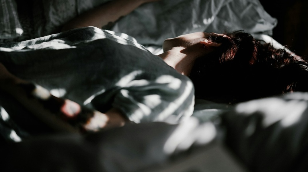 Γυναίκα ξαπλωμένη σε κρεβάτι με το πρόσωπό της γυρισμένο από την αντίθεση πλευρά από εκείνη που βρίσκεται ο φακός
