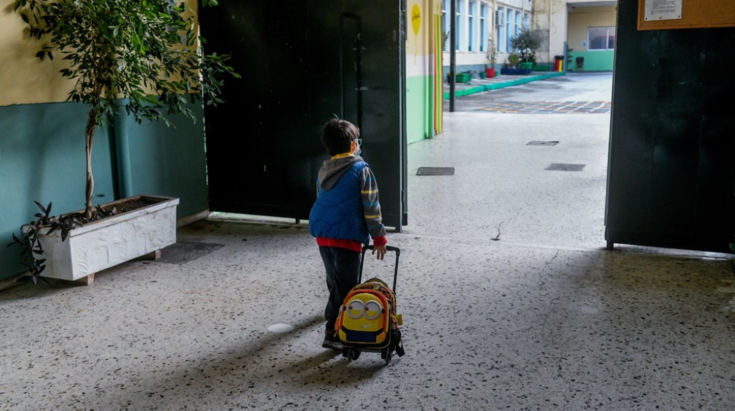 Παιδάκι με τη σχολική του τσάντα ρίχνει μία ματιά στην αυλή του σχολείου του