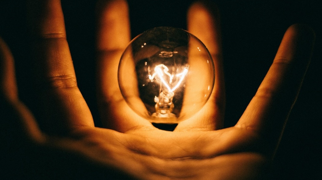 Αναμμένη λάμπα ανάμεσα στα δάχτυλα ενός χεριού