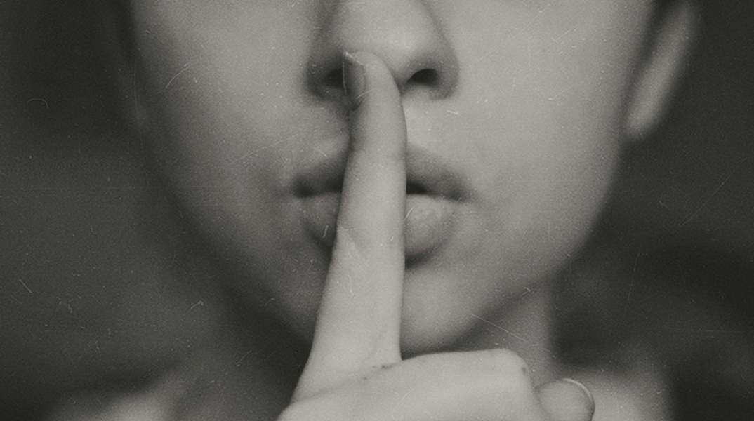 Γυναίκα κρατά το δάχτυλό της μπροστά από το κλειστό στόμα της ζητώντας ησυχία