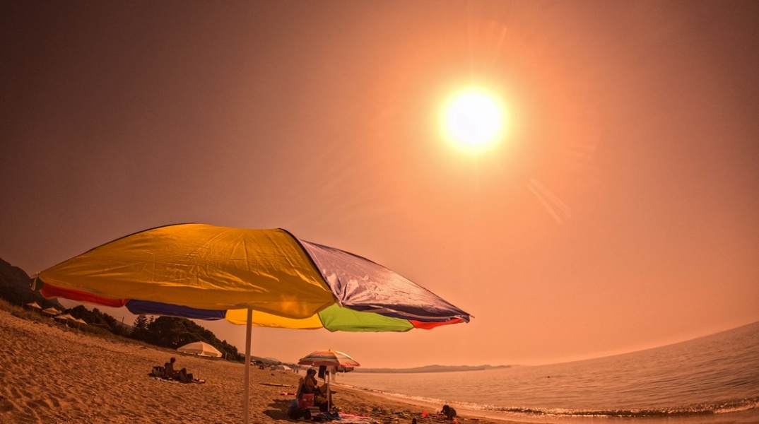Ομπρέλα σε παραλία και λουόμενοι υπό τον καυτό ήλιο