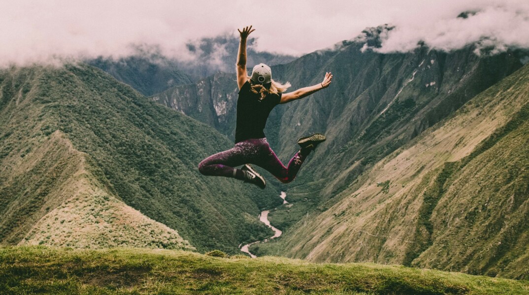 Γυναίκα πηδά στον αέρα χαρούμενη σε βουνό