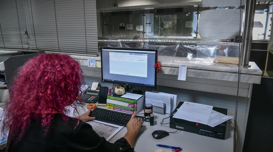 Γυναίκα με κόκκινα μαλλιά πλάτη στον φακό σε υπηρεσία συντάσσει φορολογική δήλωση στον υπολογιστή της