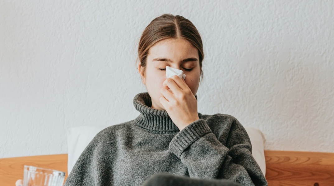 Γυναίκα ξαπλωμένη στο κρεβάτι με ίωση που φυσά τη μύτη της