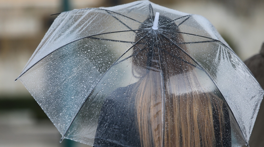 Γυναίκα κρατά ομπρέλα για να προστατευτεί από τη βροχή