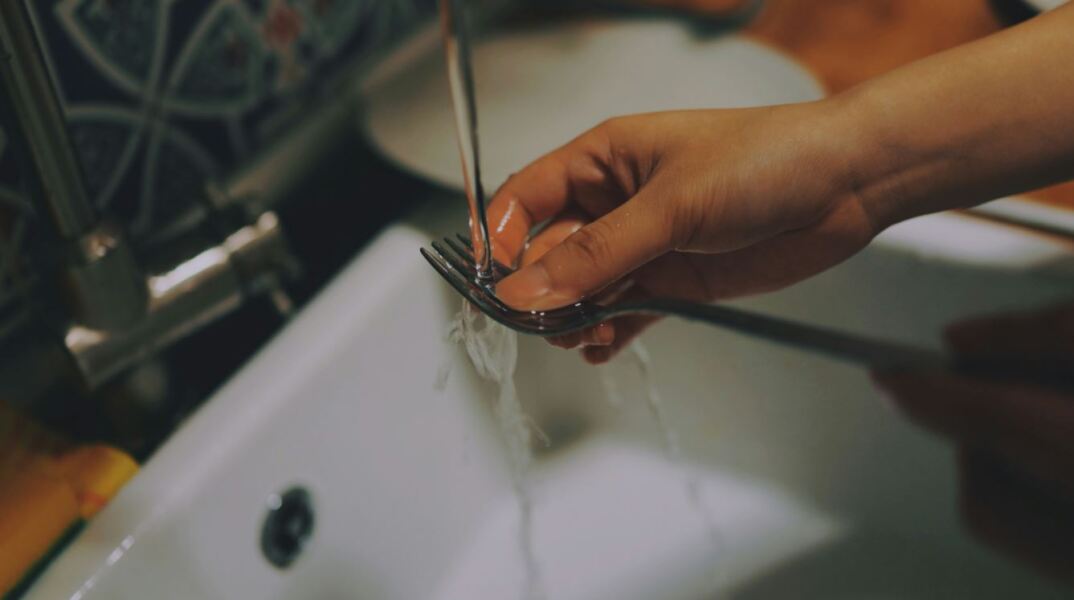 Χέρι ξεπλένει πιρούνι με νερό