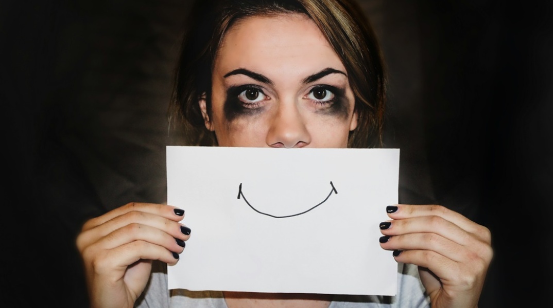 Γυναίκα που κρύβει την κακοποίησή της πίσω από ένα χαρτί με ζωγραφισμένο ένα χαμόγελο