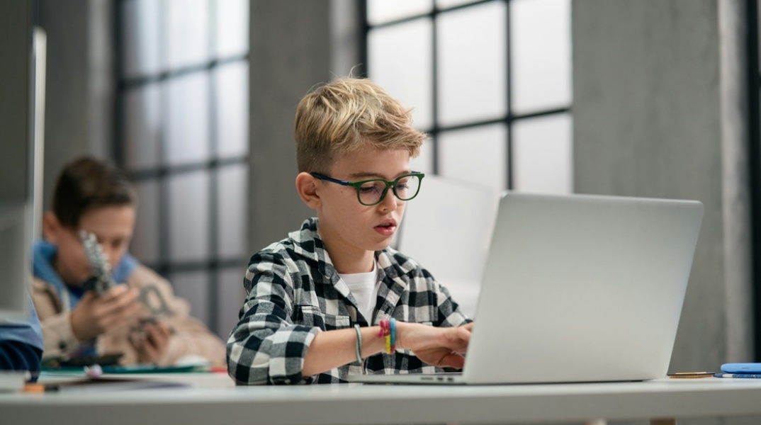 Μαθητής καθισμένος στο θρανίο του κάνει χρήση λάπτοπ
