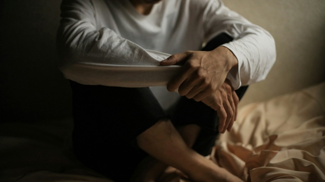 Άτομο καθισμένο στο κρεβάτι που πιάνει με τα χέρια του, τα πόδια του