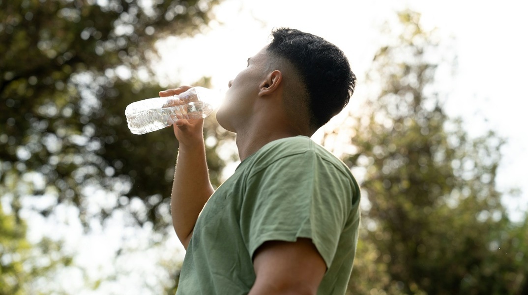 Άνδρας που έχει ιδρώσει από τιος υψηλές θερμοκρασίες, δροσίζεται πίνοντας νερό