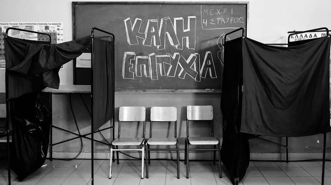 Ασπρόμαυρη φωτογραφία από εκλογικό κέντρο σε πίνακα στον οποίο γράφει «Καλή Επιτυχία»
