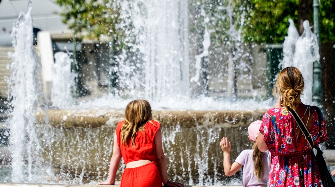 Παιδιά με τη μητέρα τους στέκονται μπροστά από το σιντριβάνι του Συντάγματος για λίγες στιγμές δροσιάς