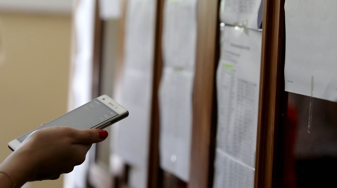 Αναρτημένες βαθμολογίες των Πανελληνίων 2024 και μαθητής που με κινητό υπολογίζει τα μόρια 