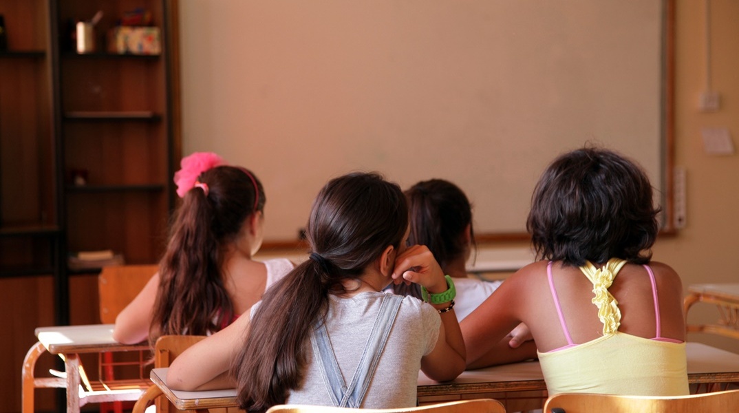 Μαθήτριες κάθονται στο θρανίο τους μέσα στη σχολική αίθουσα, με πλάτη στον φακό