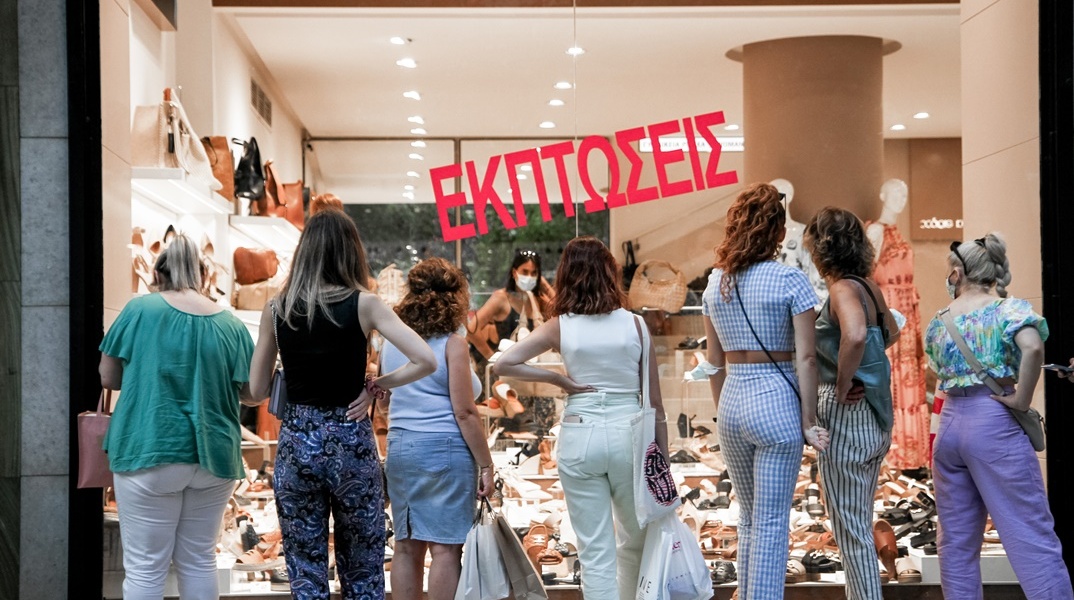 Κυρίες μπροστά από βιτρίνα καταστήματος με προϊόντα σε έκπτωση