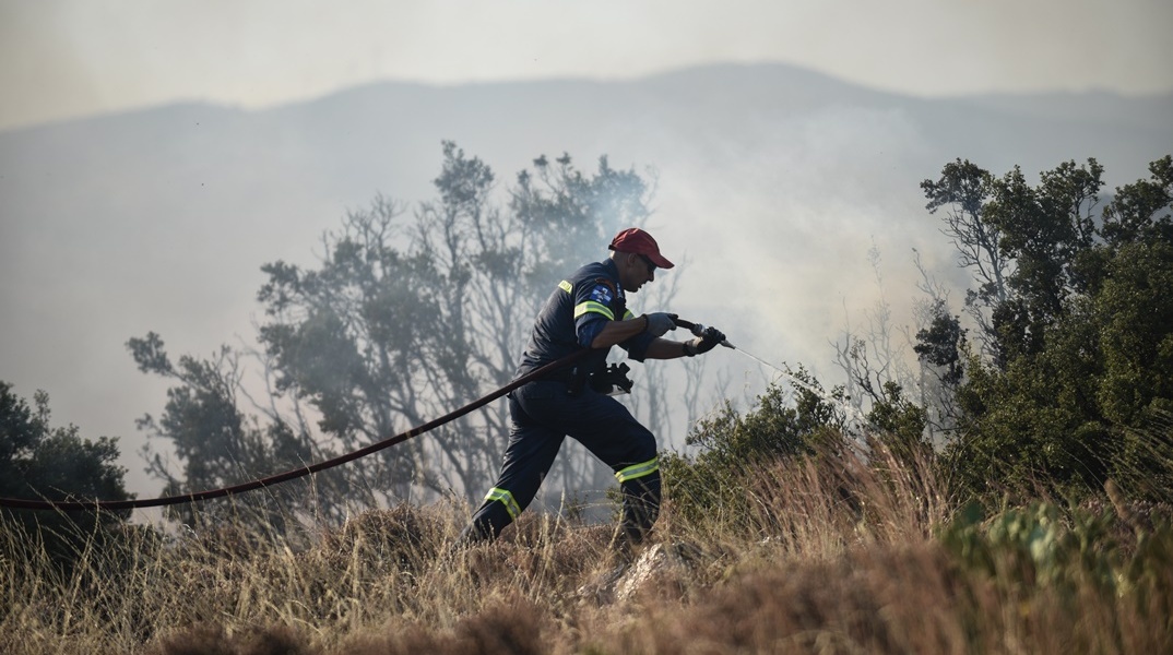 Πυροσβέστης με τη μάνικα ανά χείρας επιχειρεί για την κατάσβεσης φωτιάς