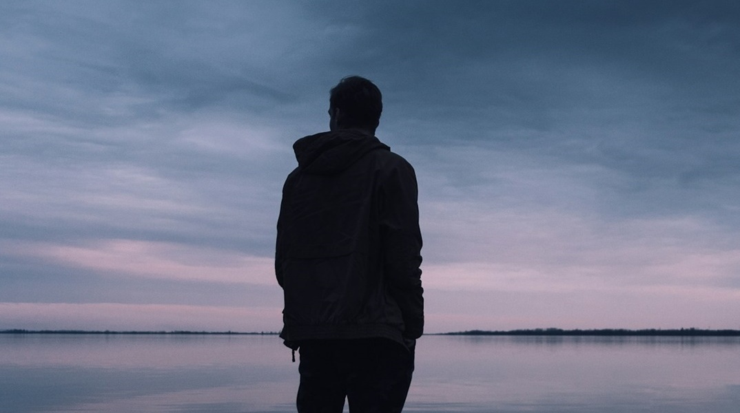 Νεαρό άτομο κοιτά τον ορίζοντα γυρισμένο πλάτη στον φακό