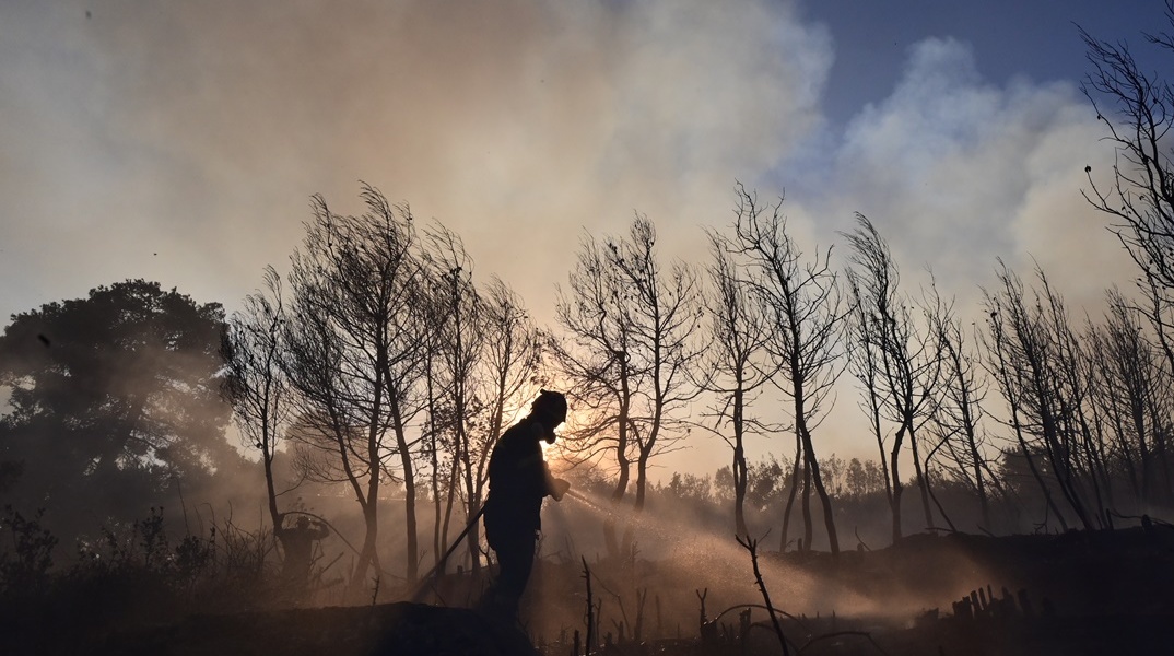 Σκιά πυροσβέστη σε περιοχή που έχει καεί από φωτιά και υπάρχουν καπνοί