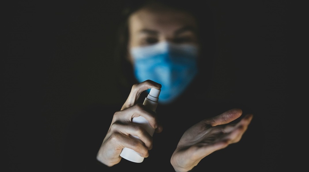 Γυναίκα βάζει αντισηπτικό στα χέρια της και διακρίνεται ότι φορά μάσκα προστασίας