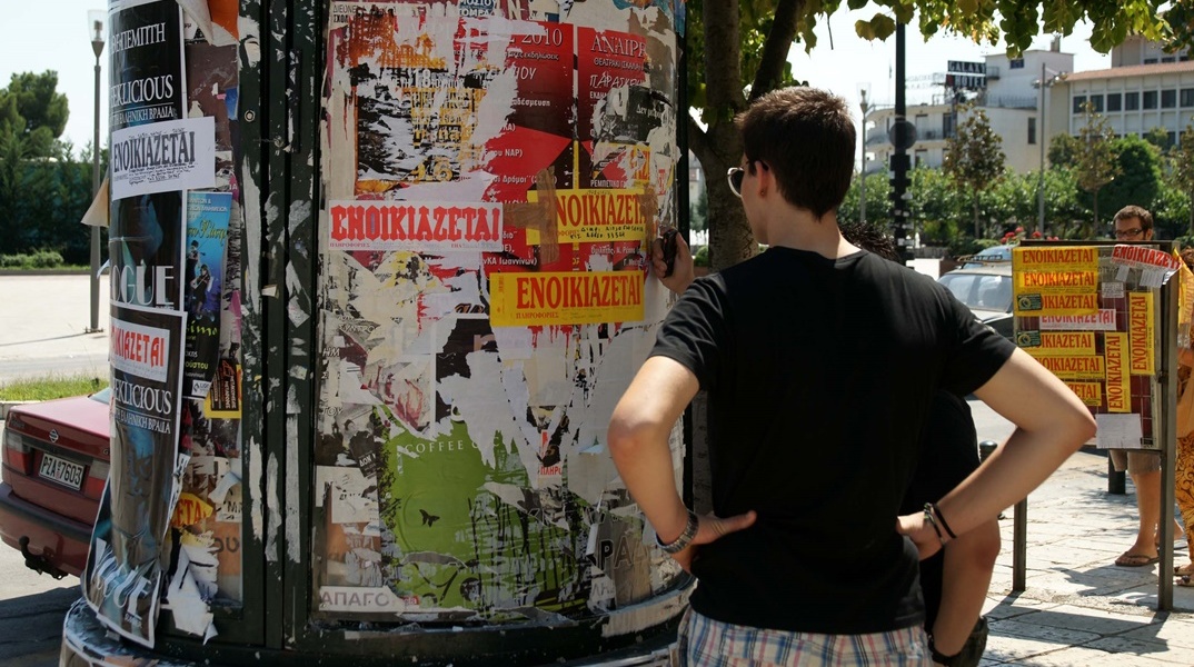 Ενοικιαστήρια σε κολώνα και νεαρό άτομο που κοιτά ενοικιαστήρια