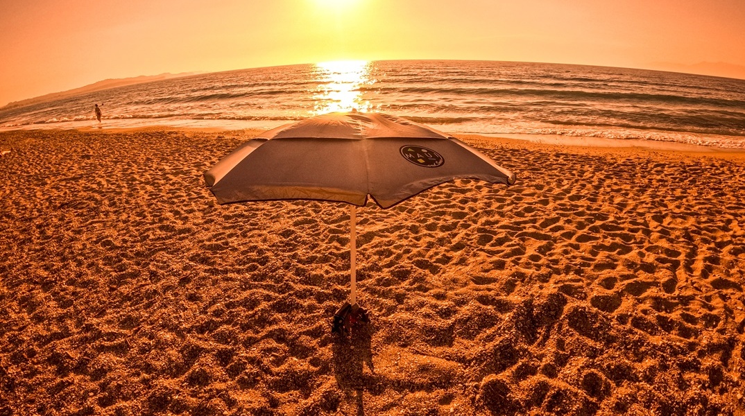 Φωτογραφία από παραλία εν μέσω καύσωνα με τον φακό να καταγράφει τον ήλιο και ομπρέλα σε παραλία