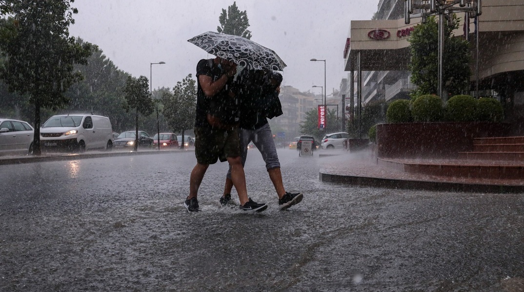 Άτομα προστεύονται από την καταρρακτώδη βροχή με ομπρέλα