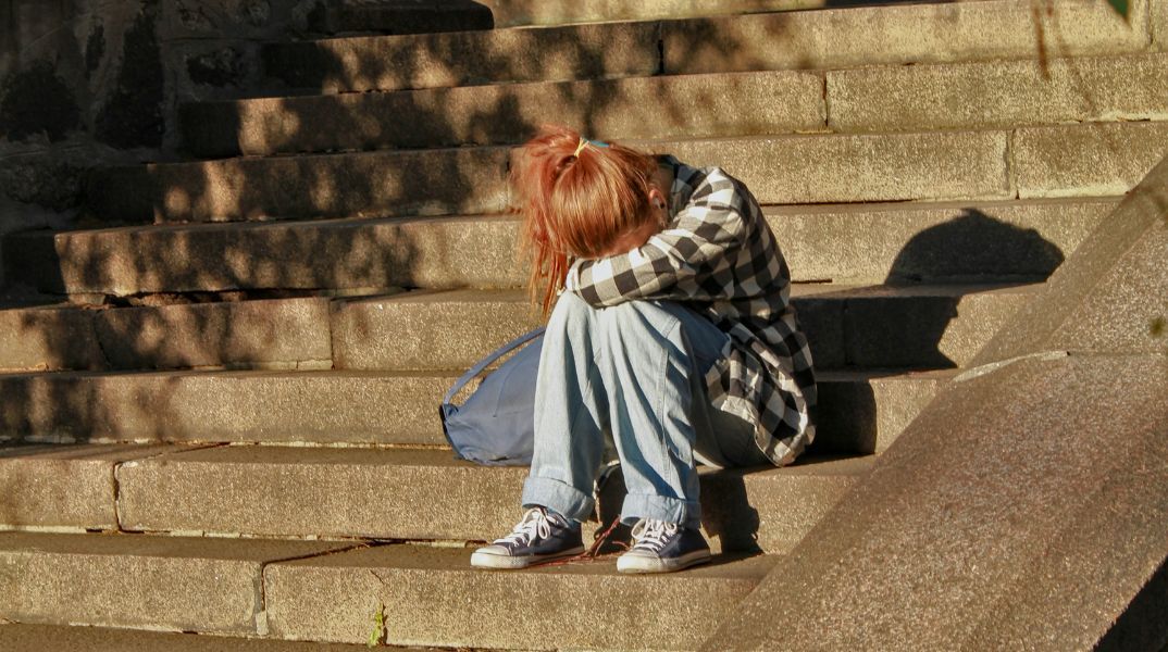 Κορίτσι καθισμένο σε σκαλιά, έχει κρύψει το κεφάλι της στα γόνατά της