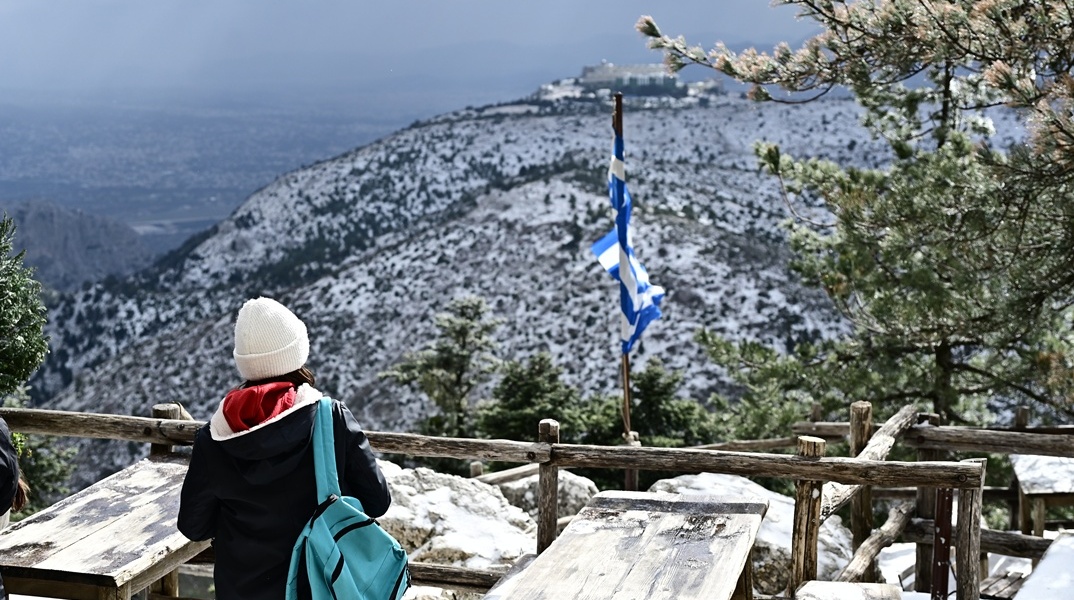 Χιόνια στην Πάρνηθα και άτομο ντυμένο με χειμωνιάτικα ρούχα που απολαμβάνει τη θέα