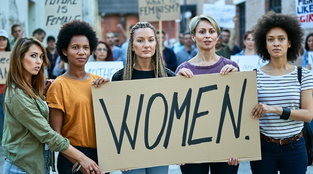 Γυναίκα με χαρτόνι που γράφει στα αγγλικά τη λέξη «Γυναίκες»