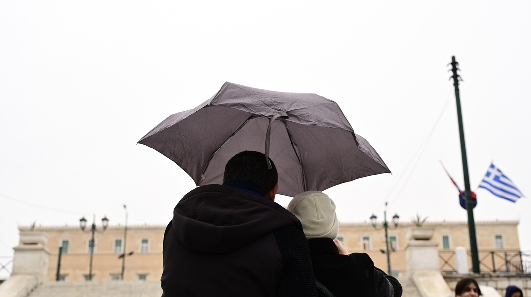 Πολίτες με ομπρέλα προστατεύονται από τη βροχή μπροστά από τη Βουλή