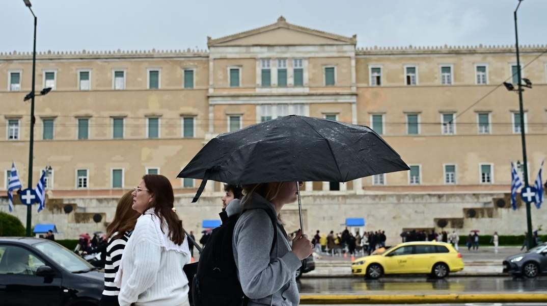 Πολίτες με ομπρέλα προστατεύονται από τη βροχή στο κέντρο της Αθήνας