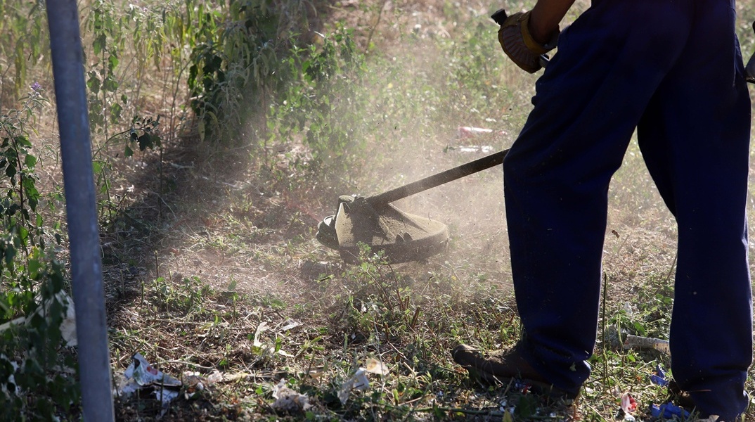 Εργάτης καθαρίζει με χορτοκοπτικό οικόπεδο