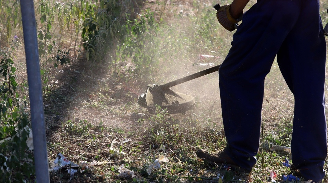 Άτομο καθαρίζει οικόπεδο από τα χορτάρια