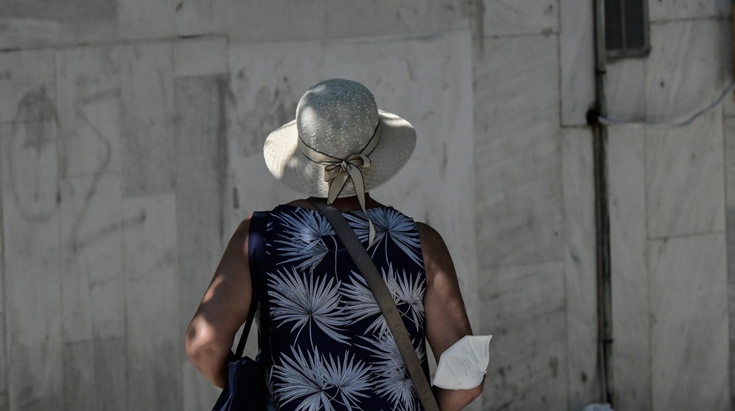 Γυναίκα με γυρισμένη πλάτη στον φακό και τη μάσκα προστασίας από τον κορωνοϊό αφημένη στον αγκώνα