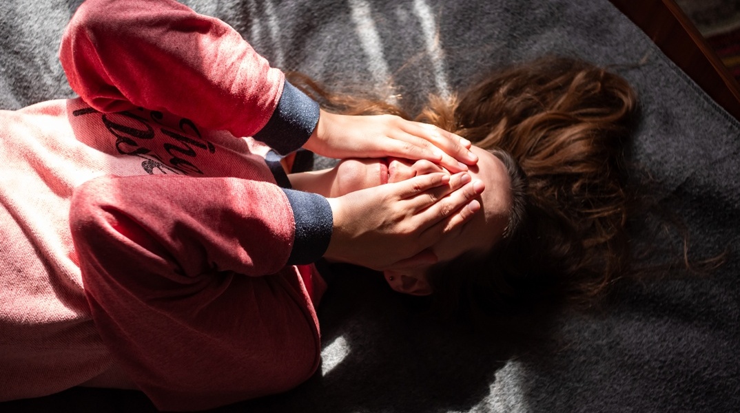 Κορίτσι που κρύβει το πρόσωπό του ενώ είναι ξαπλωμένο σε κρεβάτι