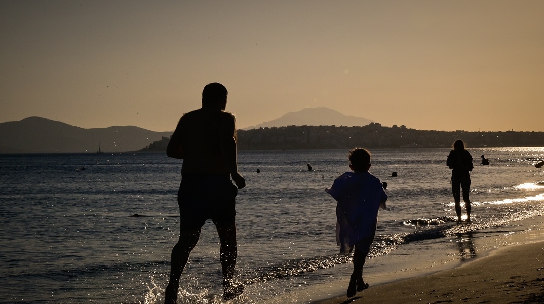 Πατέρας και παιδί που τρέχουν στην ακροθαλασσιά αναζητώντας λίγες στιγμές δροσιάς εν μέσω καύσωνα