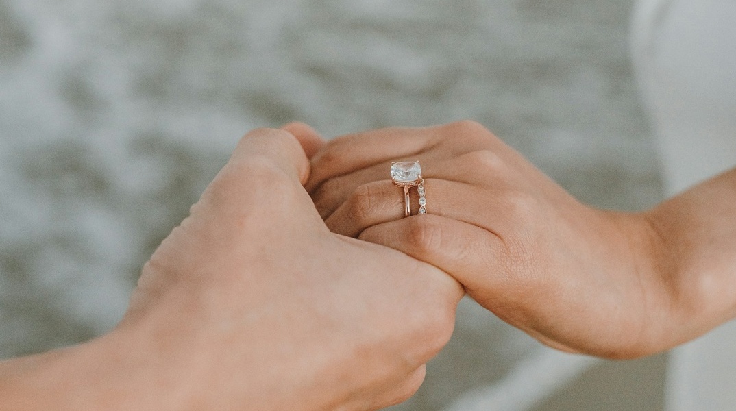 Χέρι άνδρα κρατά χέρι γυναίκας με δαχτυλίδι, εικόνα που μας δείχνει ότι έγινε πρόταση γάμου