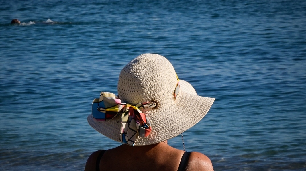 Γυναίκα με καπέλο κάθεται σε παγκάκι εν μέσω καύσωνα