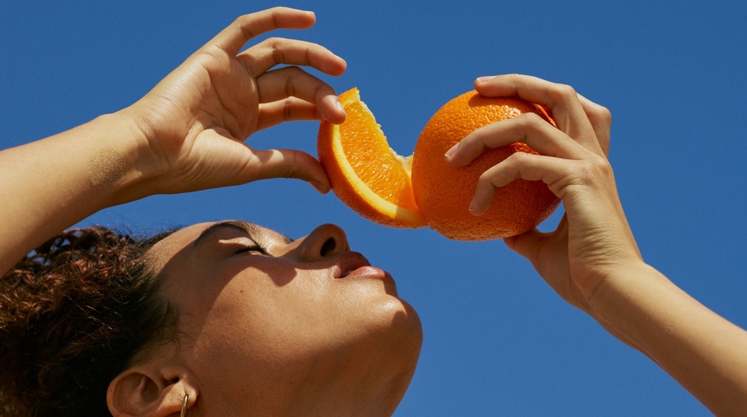 Κοπέλα στον ήλιο με κομμένο πορτοκάλι πάνω από το πρόσωπό της