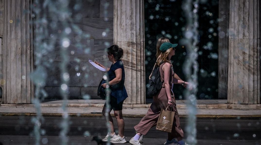 Πολίτες περπατούν πίσω από σιντριβάνι