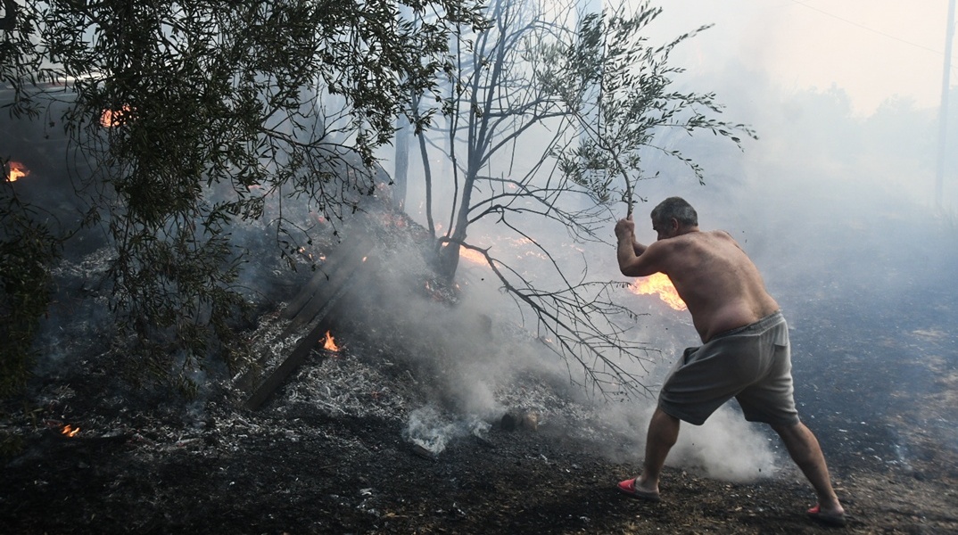 Άτομο επιχειρεί με κλαδί για την κατάσβεση φωτιάς