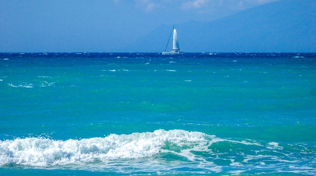 Κυματάκια σε παραλία και στο βάθος ένα ιστιοφόρο